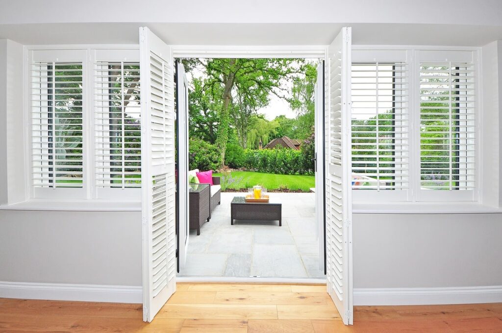 Open french doors and plantation shutters in a room with a view to the outside patio.